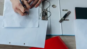 An adult writing in a binder at a desk with office supplies.